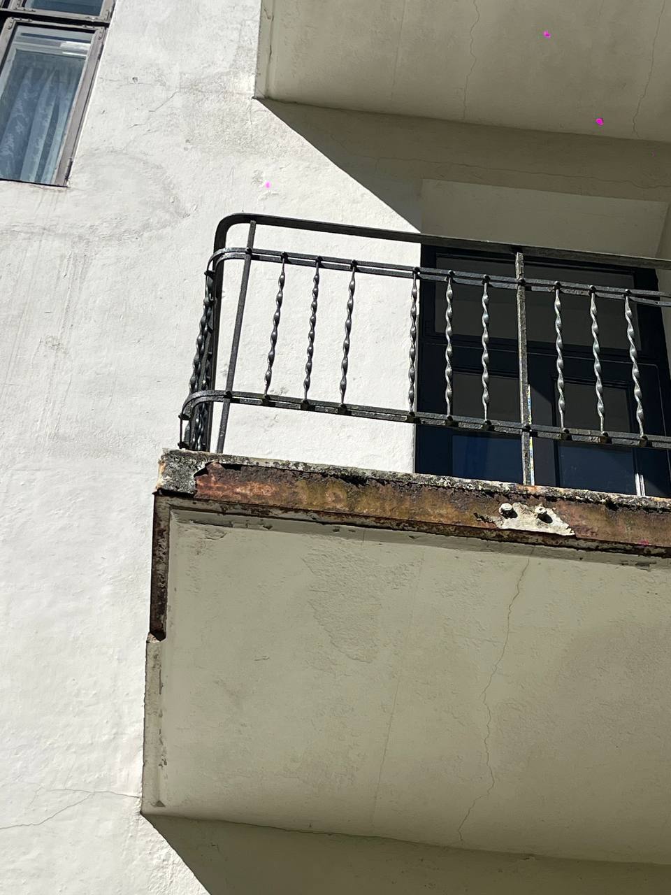 Nærbilde av balkong med rustent rekkverk, avskallet betongkant og sprekker i undersiden