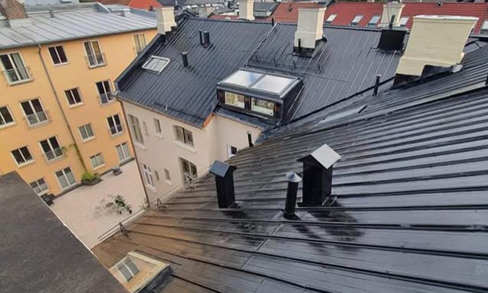 Svart metalltak på bygård med piper, takvinduer og gårdsrom